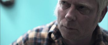 Movie still from “Down Terrace” (2009), directed by Ben Wheatley – An older man wearing a checkered button up shirt; Extreme Close Up shot, Over the shoulder angle
