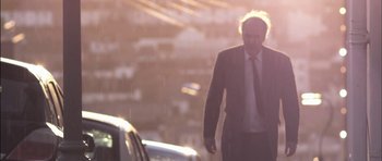 Movie still from “Down Terrace” (2009), directed by Ben Wheatley – A man in a suit and tie walking down a street; Medium shot, Low angle