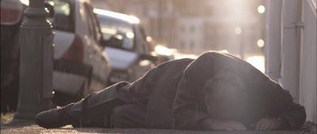 Movie still from “Down Terrace” (2009), directed by Ben Wheatley – A person laying on the ground on the side of the road; Wide shot, Low angle