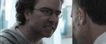 Movie still from “Down Terrace” (2009), directed by Ben Wheatley – A person wearing glasses and a white shirt; Close Up shot, Over the shoulder angle