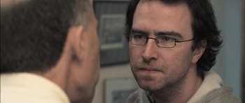 Movie still from “Down Terrace” (2009), directed by Ben Wheatley – A man wearing glasses is looking at another man; Close Up shot, Over the shoulder angle