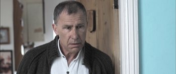 Movie still from “Down Terrace” (2009), directed by Ben Wheatley – An older man wearing a white shirt and a sweater; Close Up shot, Over the shoulder angle