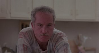 Movie still from “Down and Out in Beverly Hills” (1986), directed by Paul Mazursky – An older man with gray hair and a mustache is sitting in a kitchen; Close Up shot, Low angle