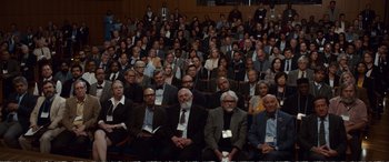 Movie still from “Downsizing” (2017), directed by Alexander Payne – A large group of people sitting in front of an audience; Wide shot, High angle