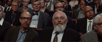 Movie still from “Downsizing” (2017), directed by Alexander Payne – A man with a beard and glasses in a crowd of people; Medium shot, Over the shoulder angle