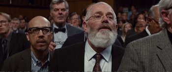 Movie still from “Downsizing” (2017), directed by Alexander Payne – An old man with a beard and glasses in a suit and tie; Close Up shot, Over the shoulder angle