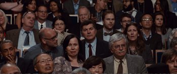 Movie still from “Downsizing” (2017), directed by Alexander Payne – A group of people sitting in front of each other; Medium shot, Over the shoulder angle