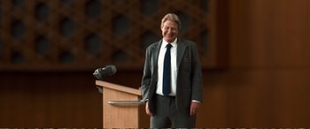 Movie still from “Downsizing” (2017), directed by Alexander Payne – A man standing at a podium in front of a microphone; Medium shot, Low angle