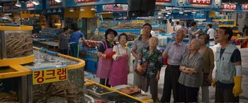 Movie still from “Downsizing” (2017), directed by Alexander Payne – A group of people standing in front of a fish market; Wide shot, High angle