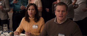 Movie still from “Downsizing” (2017), directed by Alexander Payne – A man and a woman sitting next to each other in a room; Medium shot, Over the shoulder angle