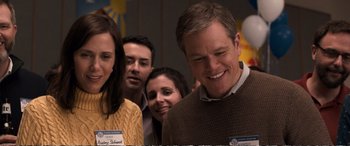 Movie still from “Downsizing” (2017), directed by Alexander Payne – A group of people that are standing in a room together; Medium shot, Over the shoulder angle