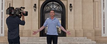 Movie still from “Downsizing” (2017), directed by Alexander Payne – A man standing in front of a building with his arms outstretched; Wide shot, Low angle