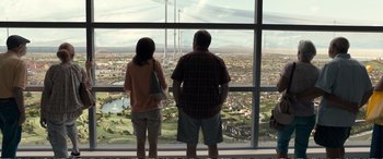Movie still from “Downsizing” (2017), directed by Alexander Payne – A man and a woman looking out of a window at a city skyline; Wide shot, Over the shoulder angle