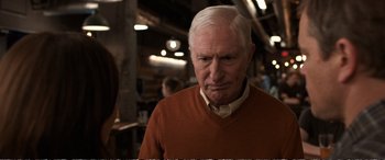Movie still from “Downsizing” (2017), directed by Alexander Payne – An older man in an orange sweater looks at the camera; Close Up shot, Over the shoulder angle