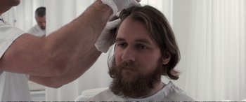Movie still from “Downsizing” (2017), directed by Alexander Payne – A man with long hair and a long beard is getting his hair cut by another man; Close Up shot, Over the shoulder angle