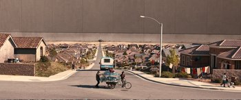 Movie still from “Downsizing” (2017), directed by Alexander Payne – Two people standing on the side of the road next to a bike; Extreme Wide shot, High angle