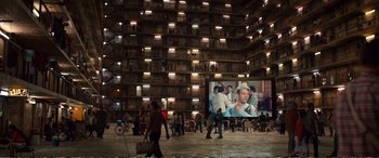 Movie still from “Downsizing” (2017), directed by Alexander Payne – People are gathered in an open area in front of a large screen; Extreme Wide shot, High angle