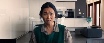 Movie still from “Downsizing” (2017), directed by Alexander Payne – A woman in a green shirt is standing in front of a white table; Close Up shot, High angle