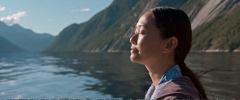 A woman with her eyes closed near a body of water