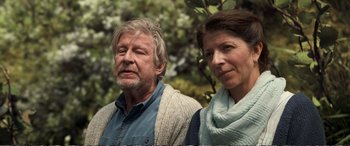 Movie still from “Downsizing” (2017), directed by Alexander Payne – An older man and a younger woman standing next to each other in a wooded area; Close Up shot, Over the shoulder angle