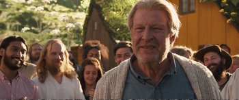Movie still from “Downsizing” (2017), directed by Alexander Payne – An old man with long white hair and a beard standing in front of a group of young people; Close Up shot, Over the shoulder angle