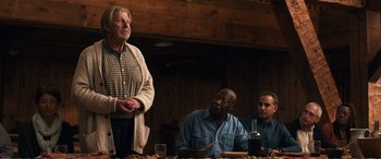 Movie still from “Downsizing” (2017), directed by Alexander Payne – A man standing next to two other men at a table; Medium shot, Over the shoulder angle