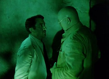 Movie still from “Dr. Cyclops” (1940), directed by Ernest B. Schoedsack – Two men are talking in a dimly - lit room; Medium shot, Over the shoulder angle