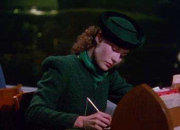 Movie still from “Dr. Cyclops” (1940), directed by Ernest B. Schoedsack – A woman in a green jacket and hat writing on a piece of paper; Medium shot, Low angle