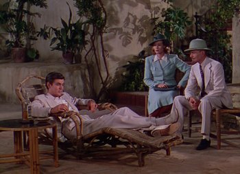 Movie still from “Dr. Cyclops” (1940), directed by Ernest B. Schoedsack – A man and two women sitting on a chair in front of another man; Wide shot, High angle