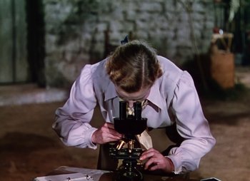 Movie still from “Dr. Cyclops” (1940), directed by Ernest B. Schoedsack – A woman looking through a microscope in a room; Medium shot, High angle