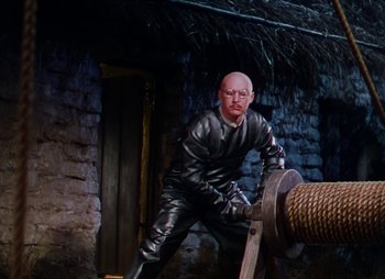 Movie still from “Dr. Cyclops” (1940), directed by Ernest B. Schoedsack – A man in a black leather outfit leaning on a rope; Medium shot, High angle