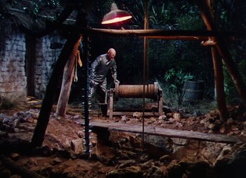 Movie still from “Dr. Cyclops” (1940), directed by Ernest B. Schoedsack – An old man in a silver suit working on a machine in the woods; Wide shot, High angle