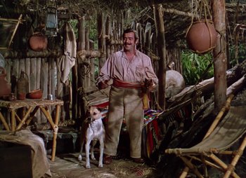 Movie still from “Dr. Cyclops” (1940), directed by Ernest B. Schoedsack – A man standing next to a dog in a hut; Wide shot, Low angle