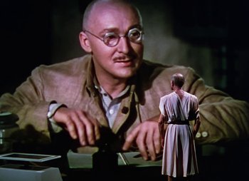 Movie still from “Dr. Cyclops” (1940), directed by Ernest B. Schoedsack – A man in a robe standing in front of an image of a bald man; Medium shot, Low angle