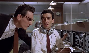 Movie still from “Dr. No” (1962), directed by Terence Young – Two men wearing headphones and talking to each other in an office setting; Medium shot, Low angle