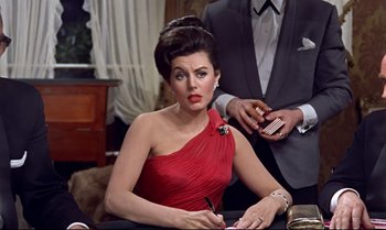 Movie still from “Dr. No” (1962), directed by Terence Young – A woman in a red dress sitting at a table with a man in a gray suit; Medium shot, Over the shoulder angle