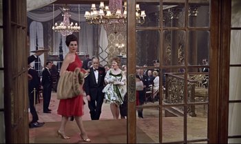 Movie still from “Dr. No” (1962), directed by Terence Young – A woman in a red dress walking in front of a crowd; Wide shot, High angle