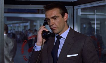 Movie still from “Dr. No” (1962), directed by Terence Young – A man in a suit and tie talking on a phone; Close Up shot, Low angle