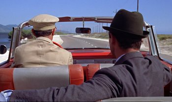 Movie still from “Dr. No” (1962), directed by Terence Young – Two men driving a red car down a street; Medium shot, Over the shoulder angle