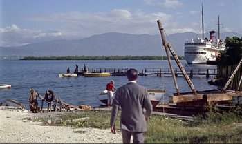 Movie still from “Dr. No” (1962), directed by Terence Young – A man in a suit standing on the shore of a body of water; Extreme Wide shot, Over the shoulder angle