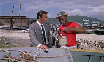 Movie still from “Dr. No” (1962), directed by Terence Young – Two men standing next to each other near a boat; Medium shot, Low angle
