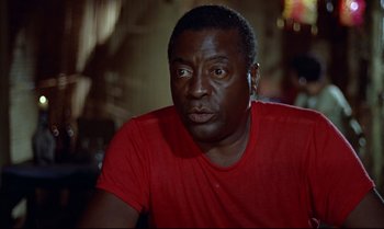 Movie still from “Dr. No” (1962), directed by Terence Young – A person wearing a red t - shirt; Close Up shot, Over the shoulder angle