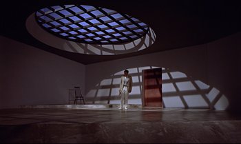 Movie still from “Dr. No” (1962), directed by Terence Young – A man standing in front of an open door in an empty room; Extreme Wide shot, Low angle