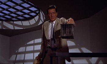 Movie still from “Dr. No” (1962), directed by Terence Young – A man in a suit and tie holding a cage; Medium shot, Low angle