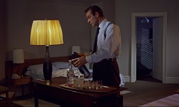 Movie still from “Dr. No” (1962), directed by Terence Young – A man standing in front of a table filled with glasses; Medium shot, Low angle
