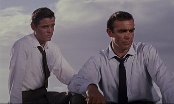 Movie still from “Dr. No” (1962), directed by Terence Young – Two men in dress shirts and ties holding hands; Medium shot, Low angle