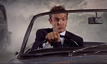 Movie still from “Dr. No” (1962), directed by Terence Young – A man in a suit and tie driving a car; Close Up shot, Low angle