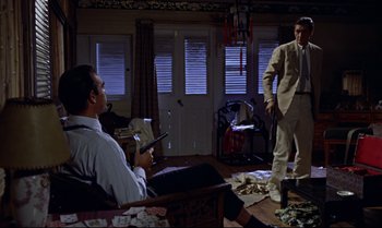 Movie still from “Dr. No” (1962), directed by Terence Young – A man in a white shirt and a man in a tan suit are in a living room; Wide shot, Low angle