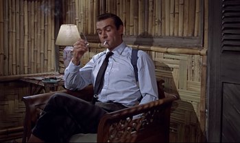 Movie still from “Dr. No” (1962), directed by Terence Young – A man sitting in a chair smoking a cigarette; Medium shot, Low angle