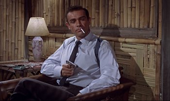 Movie still from “Dr. No” (1962), directed by Terence Young – Sean connery smoking a cigarette while sitting in a chair; Medium shot, Low angle